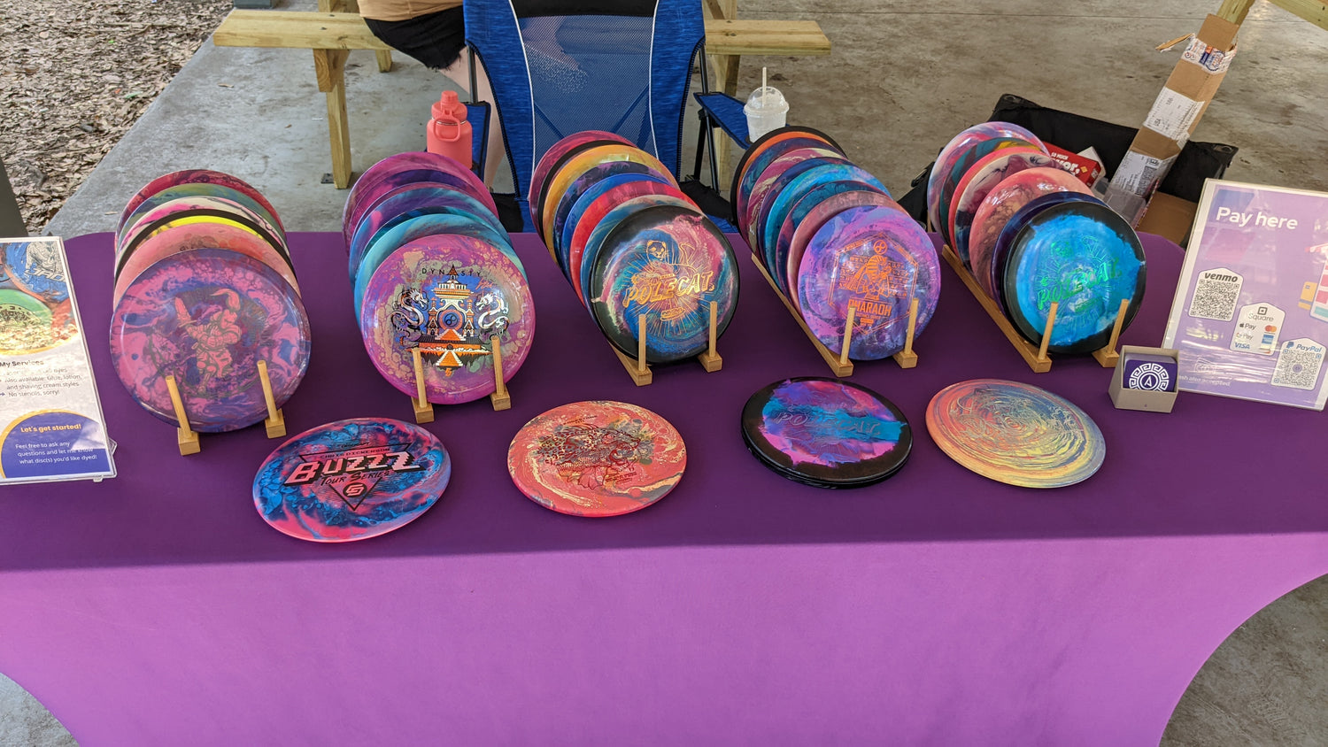 A table with dozens of hand-dyed disc golf discs displayed for sale